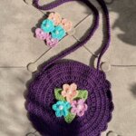handmade crochet circular purse with a long shoulder strap and colorful flower appliques