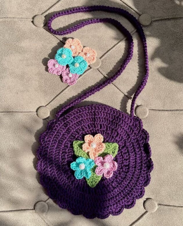 handmade crochet circular purse with a long shoulder strap and colorful flower appliques