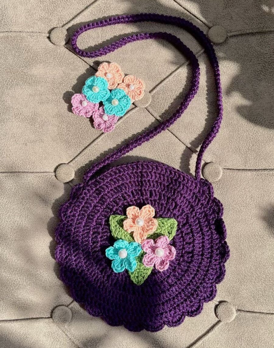 handmade crochet circular purse with a long shoulder strap and colorful flower appliques